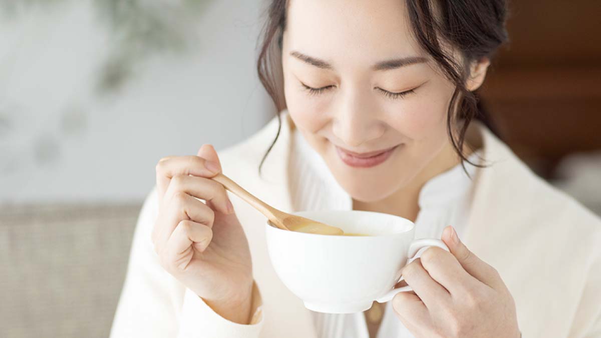 カップからスープを飲む笑顔の女性